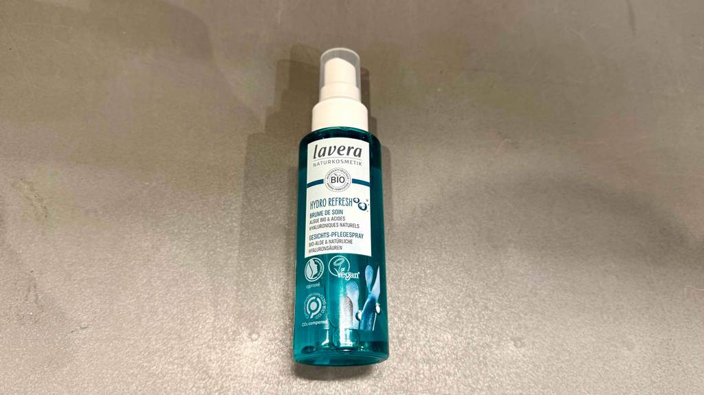 Getestetes Gesichtsspray im transparenten Pumpspender liegt auf einer grauen Oberfläche.