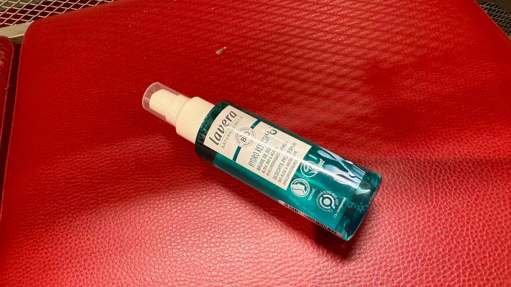 Im Test: Ein Gesichtsspray im transparenten Pumpspender liegt auf einer roten Oberfläche aus Leder.