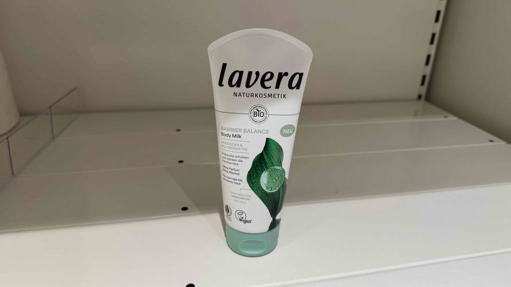 Eine Tube getestete Naturkosmetik-Bodylotion steht in einem leeren weißen Regalfach.