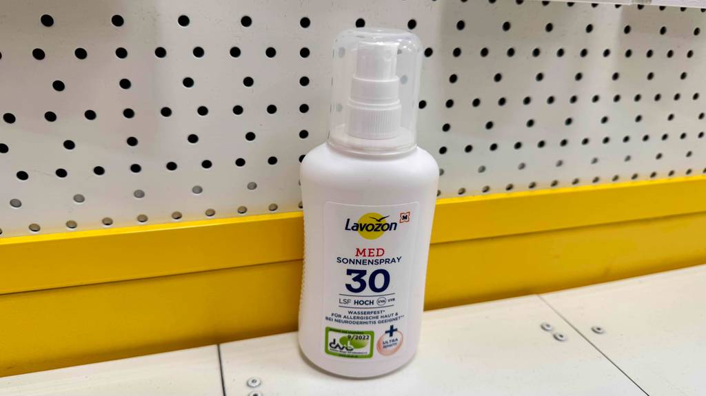 Eine Sprühflasche getestetes Sonnenspray steht vor einer gelben Leiste.