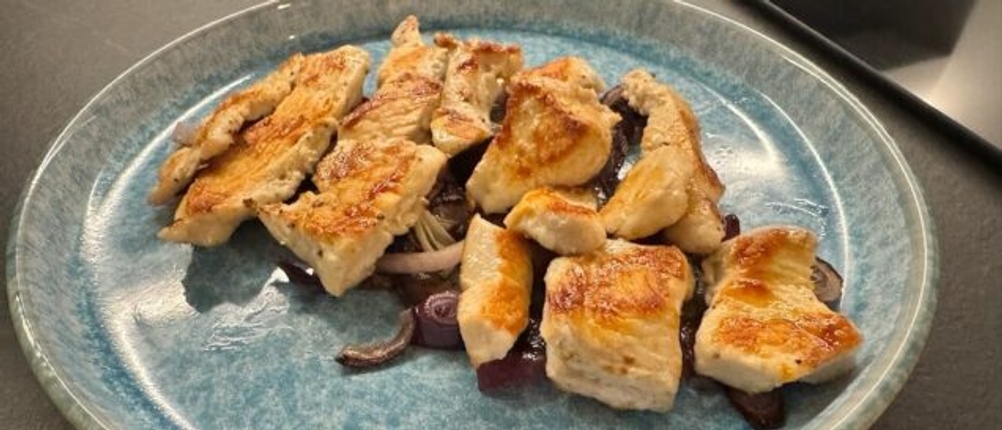 Fertig gebratenes Fleisch auf den angebratenen Zwiebeln auf einem blauen Teller