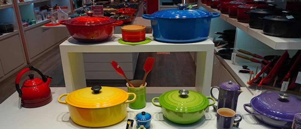 Le-Creuset-Bräter im Deko-Test: Verschiedene Bräter in unterschiedlichen Farben stehen auf einem weißen Regal.
