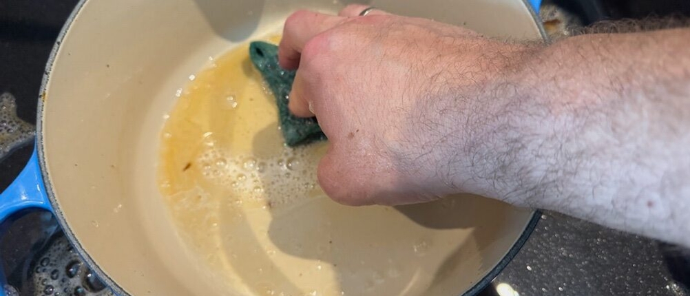 Eine Hand reinigt den Behälter des Le Creuset LS2501-2467SS mit einem Lappen und Wasser