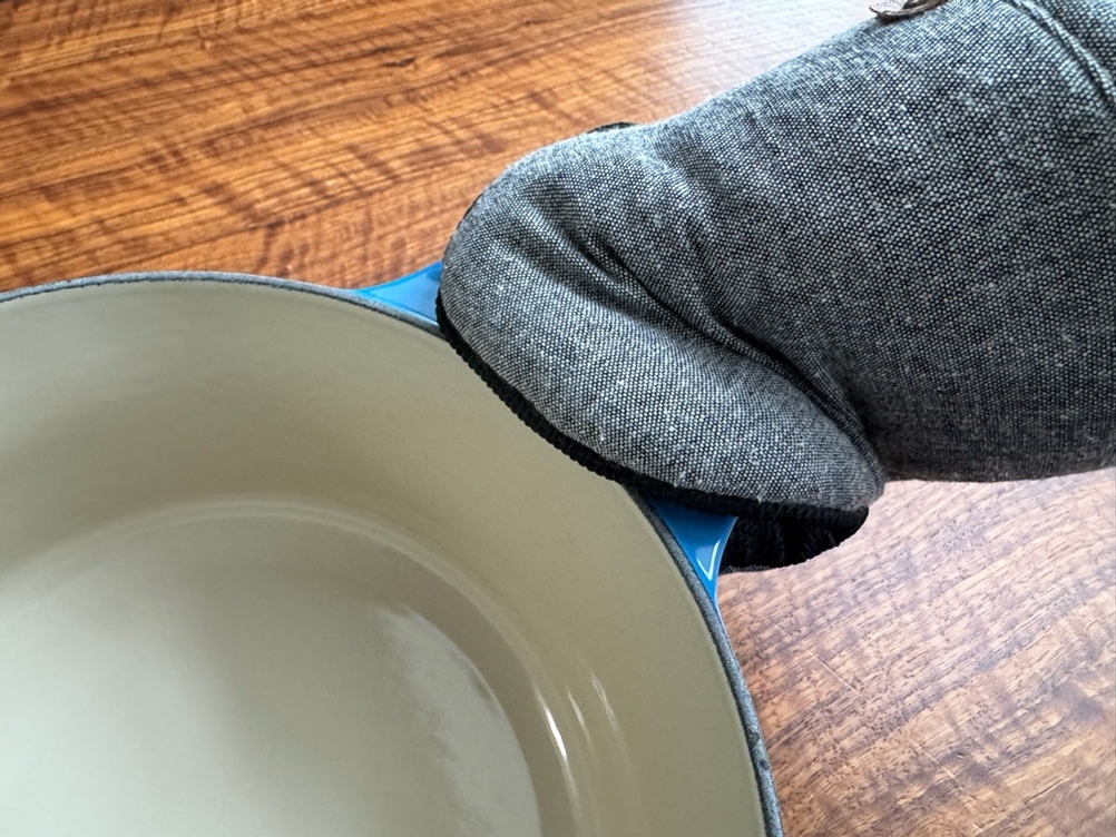 Eine Hand hält einen Griff des Le Creuset LS2501-2467SS mit einem Handschuh fest