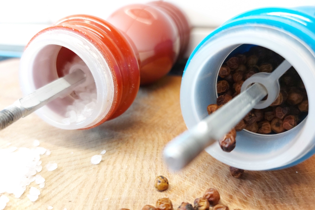 Ein getestetes Salz- und Pfeffermühlen-Set liegt mit Deckel geöffnet, davor Salz und Pfeffer.