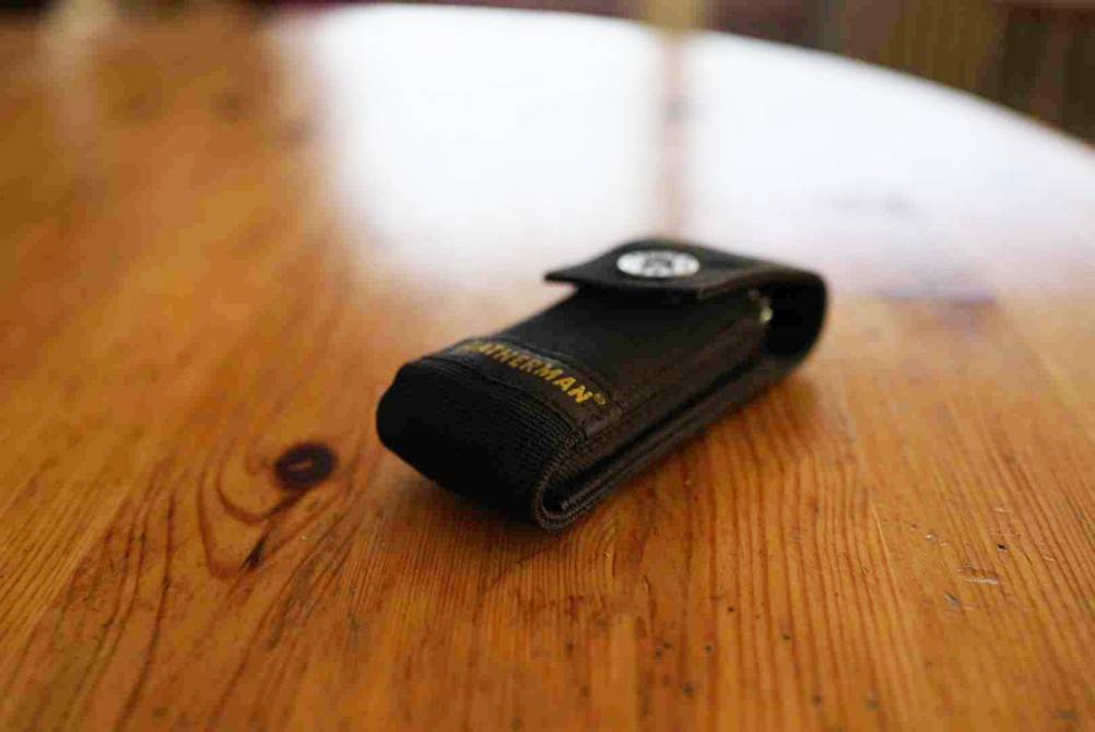 Ein getesteter Leatherman in seiner Schutztasche auf einer Holzfläche.