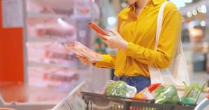 Kalorienzähler-Apps im Test: Eine Frau steht im Supermarkt und scannt den Barcode eines Produkts mit ihrer Smartphone-Kamera.