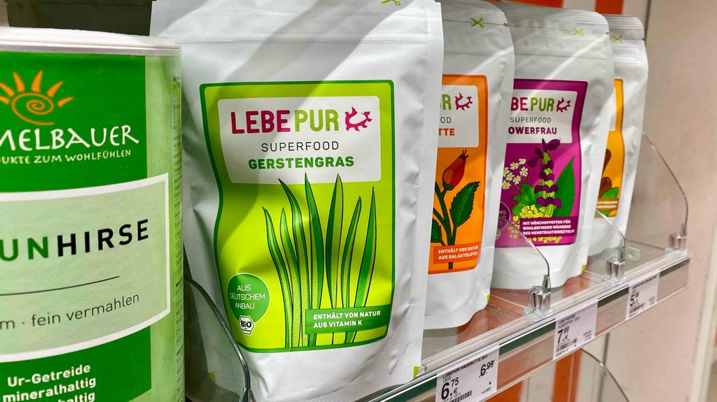 Lebepur Gerstengras im Test steht in seinem weiß-grünen Standbeutel auf einem Verkaufsregal inmitten anderer Superfoods.