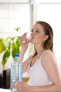 Leberkur-Test: Junge blonde Frau mit vielen Leberflecken auf der Haut im rosa Shirt und weissem Handtuch um den Hals trinkt ein Glas stilles Wasser nach dem Sport oder Fitnesstraining oder bei einer Kur.