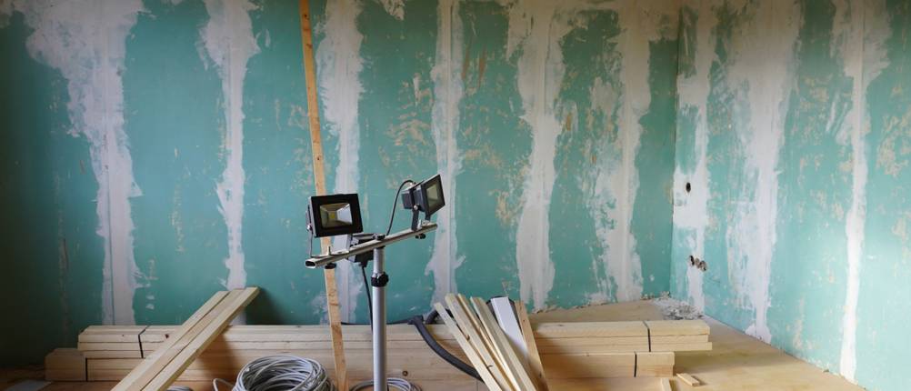 Led-Baustrahler-mit-Stativ im Test: Eine Baustelle mit rohen Wänden, Material und einem LED-Baustrahler in der Mitte mit zwei Leuchten.