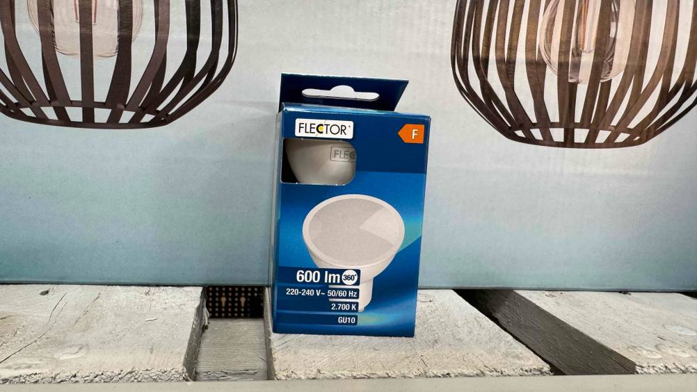 Vor einem Plakat mit Lampenschirmen steht eine Packung der getesteten LED-Lampen.