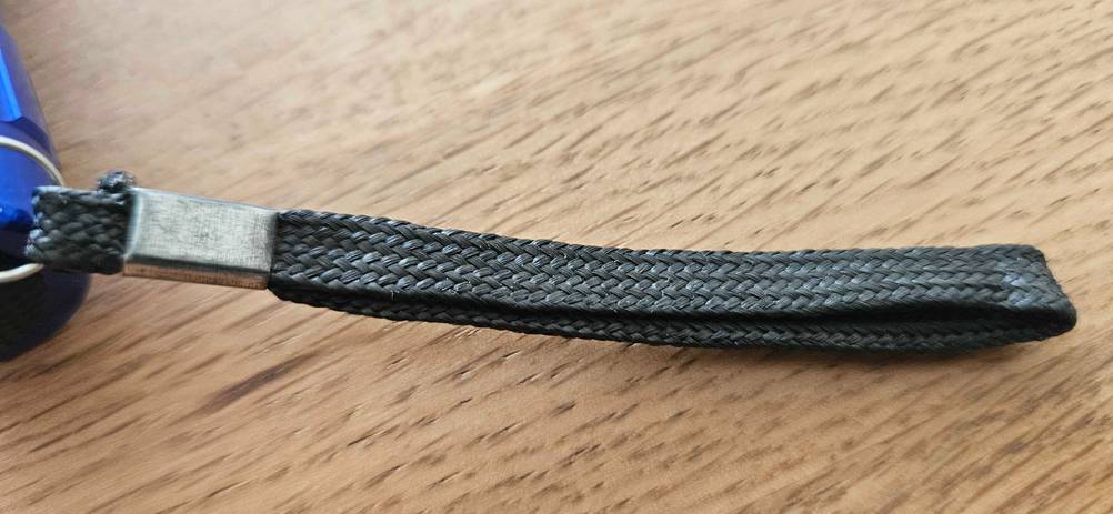 Getestet: Nahaufnahme der Halteschlaufe einer LED-Taschenlampe auf einer Holzfläche.