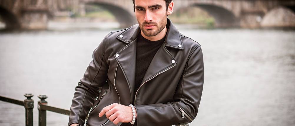 Lederjacken im Test: Mann steht an Geländer an Fluss und testet neue Lederjacke für Herren.