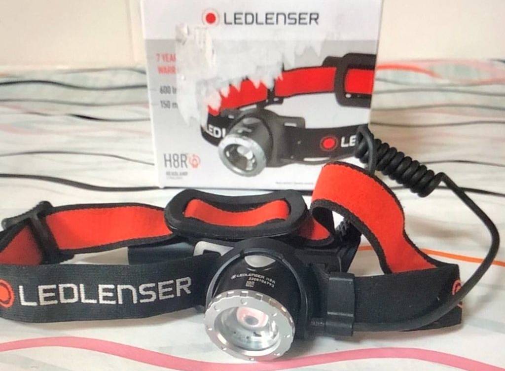 Stirnlampen-Test: ein schwarz-rotes Modell H8R der Marke Ledlenser liegt vor der Originalverpackung auf einer gemusterten Tischdecke.