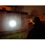 Ein Mann trägt die Ledlenser H7R Core Stirnlampe und richtet den Lichtstrahl auf eine Hauswand. Der Fokus der Lampe ist stark gebündelt sichtbar.