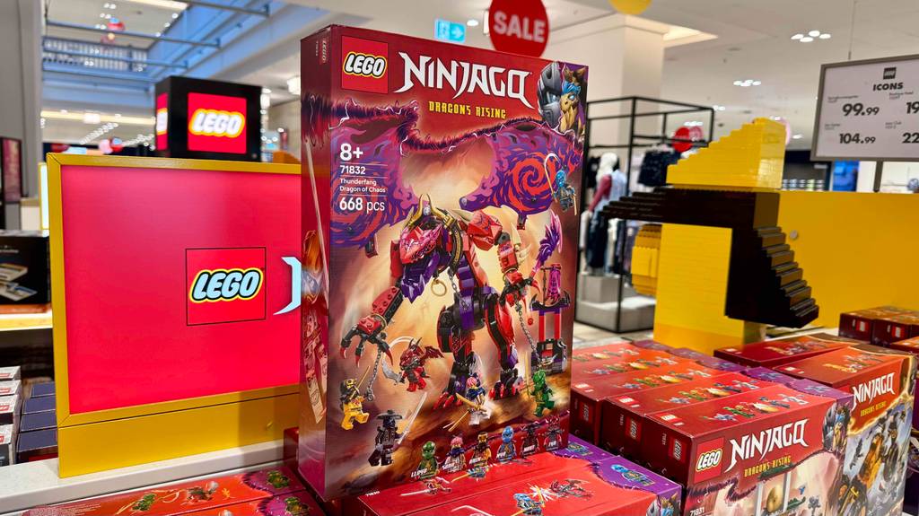 Ein verpacktes Set mit Lego-Ninjago-Figuren steht zum testen neben einem Lego-Werbeplakat.