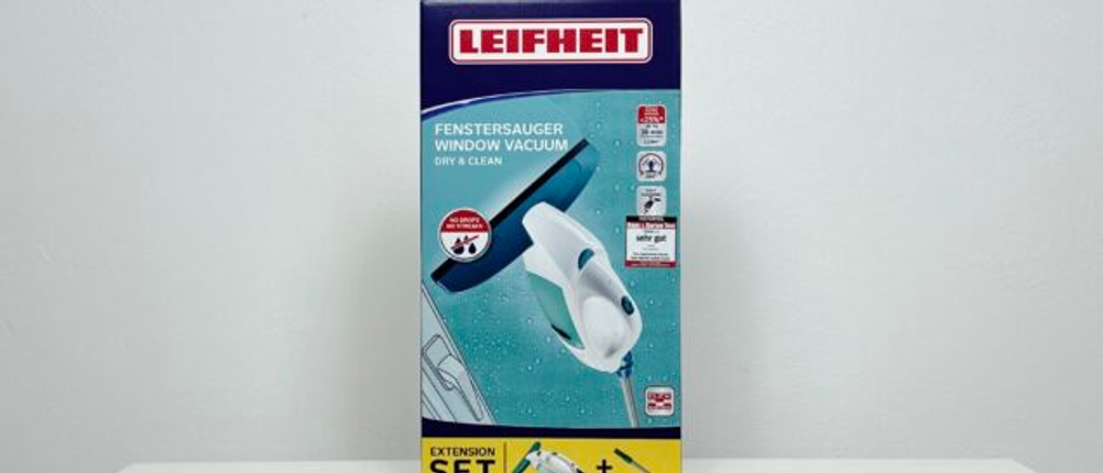 Die Verpackung des Leifheit Dry & Clean steht aufrecht auf einem weißen Tisch. Das Produkt ist in der Set-Version mit Verlängerung abgebildet.