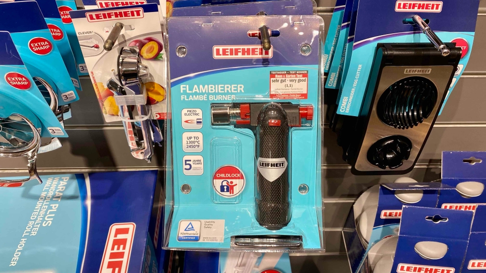 Im Test: Ein originalverpackter Flambierbrenner hängt neben anderen Produkten in einem Verkaufsregal.
