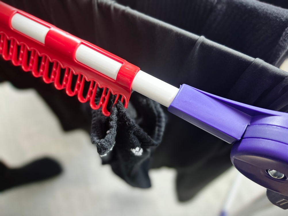 Nahaufnahme einer roten Kleinteilehalterung am Leifheit-Standtrockner 81510. Eine Socke ist darin eingehängt, weitere Wäsche hängt auf den Leinen.