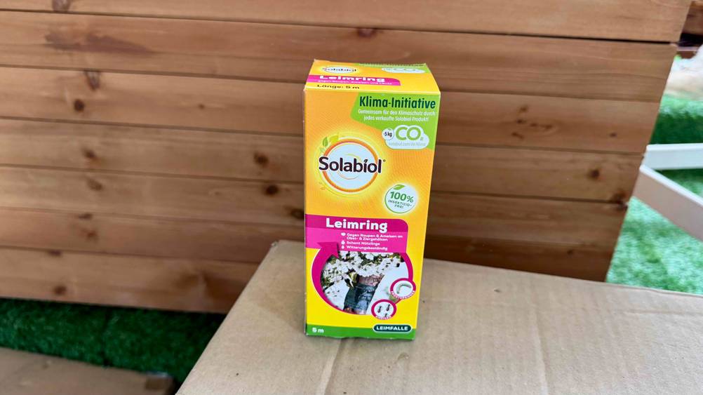 Auf einem Karton vor einer Holzbox steht eine Packung des getesteten Leimrings.