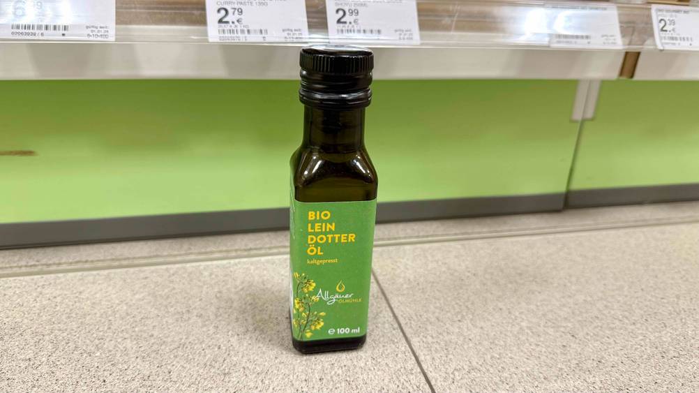 Eine Flasche des getesteten Leindotteröl vor einem Regal auf dem Boden stehend.