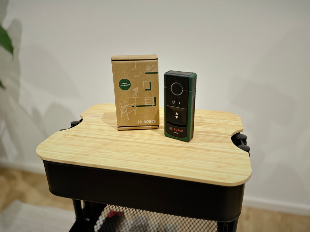 Das Produkt von Bosch steht mit der Verpackung und Zubehör auf einem hölzernen Untergrund vor einer weißen Wand.