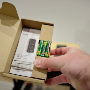 Eine Hand hält die Verpackung des Bosch-Leitungssuchers mit Zubehör.