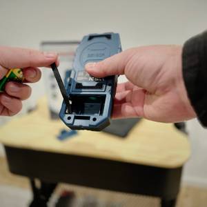 Eine Person öffnet das Batterienfach des Leitungssuchers von Hanmatek.