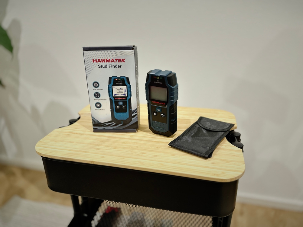 Das Produkt von Hanmatek steht mit der Verpackung und Zubehör auf einem hölzernen Untergrund vor einer weißen Wand.
