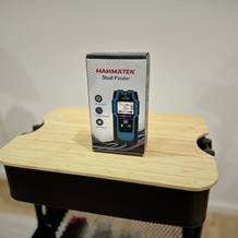 Der Leitungssucher von Hanmatek steht auf einem hölzernen Untergrund vor einer weißen Wand.