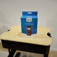 Der Leitungssucher von Testboy steht auf einem hölzernen Untergrund vor einer weißen Wand.