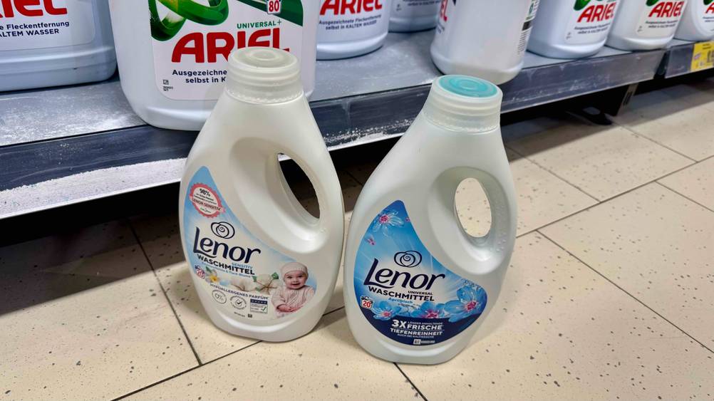 Vor einem Verkaufsregal stehen zwei unterschiedliche Flaschen des Lenor-Waschmittels im Test auf dem Boden.