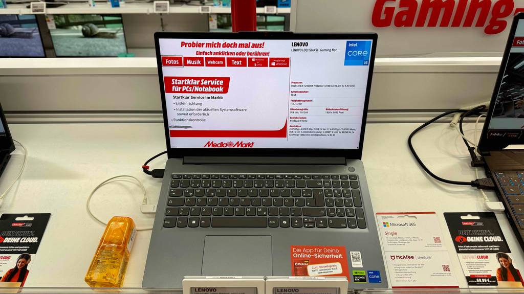 Das getestete Gaming-Laptop bis 800 Euro steht mit eingeschaltetem Bildschirm auf einem Ausstellungstisch zwischen zwei Laptops.