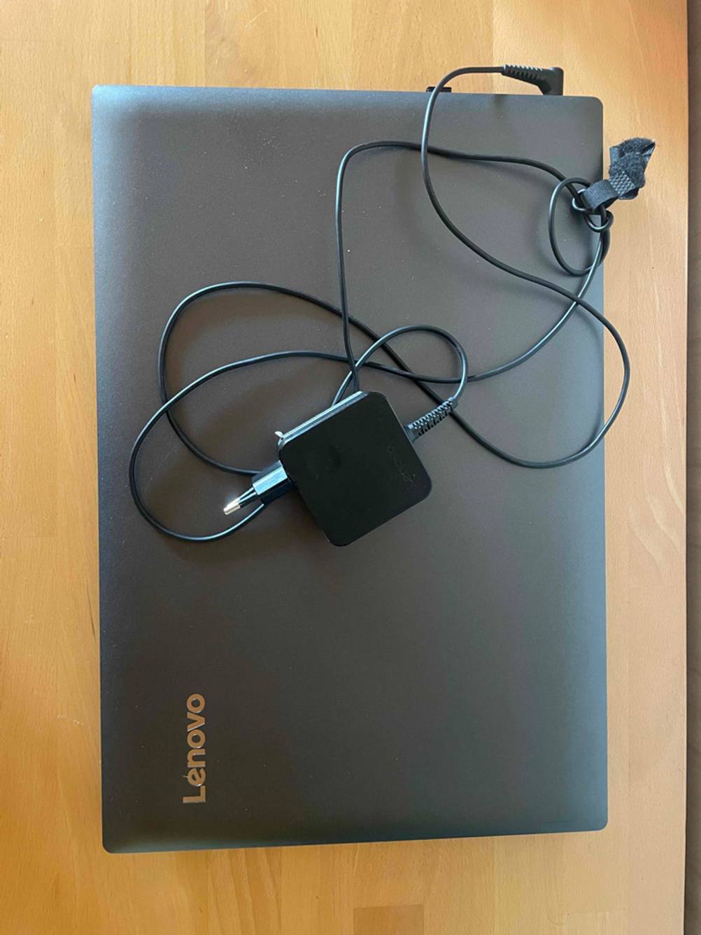 Ein getestetes Laptop mit DVD-Laufwerk liegt geschlossen mit darauf liegendem Stromkabel auf einem Tisch.