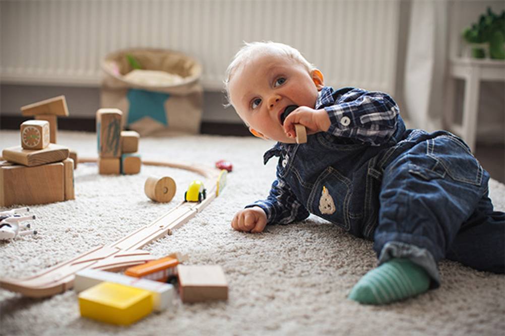 Lernspielzeug ab 1 Jahr im Test: Ein Baby das sich einen Bauklotz aus Holz in den Mund steckt.
