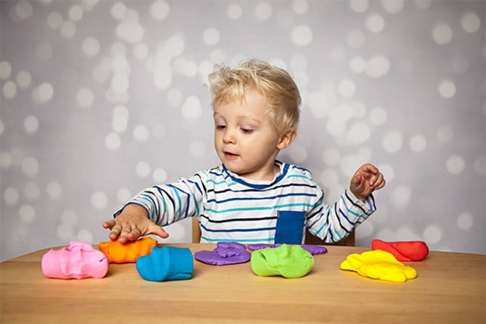 Lernspielzeug ab 1 Jahr im Test: Ein Junge der mit Knete in unterschiedlichen Farben spielt.