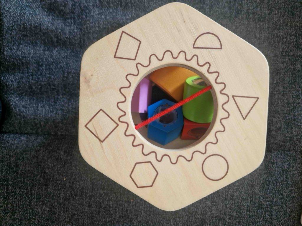 Bunte Holzbausteine in einem Holz-Lernspielzeug im Test, das auf schwarzem Teppich steht.