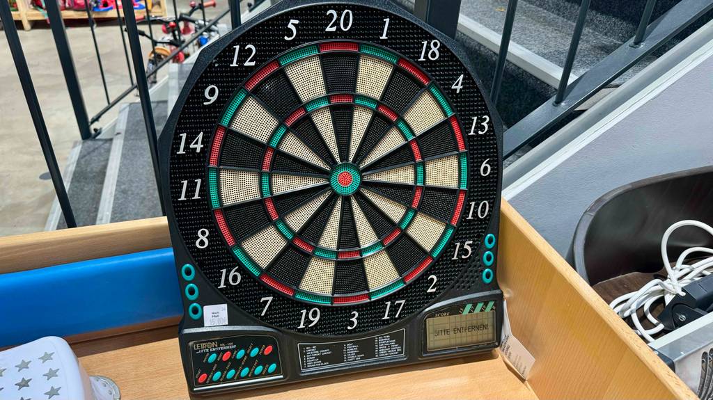 Eine elektronische Dartscheibe steht getestet in einem Holzregal.
