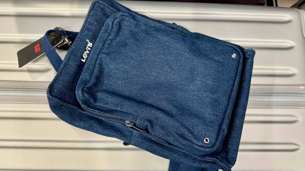 Getestet: Ein Sling-Bag in blauer Jeansausführung liegt auf einem weißen Koffer.