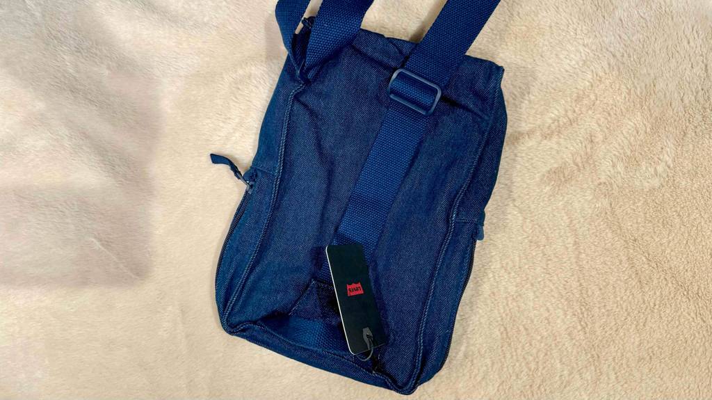 Im Test: ein Sling-Bag aus Jeansstoff liegt von hinten betrachtet auf einer beigefarbenen Fläche.