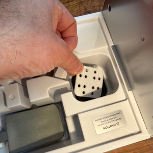 Eine Hand legt ein kleines Plättchen mit Löchern in den Levoit LV600S