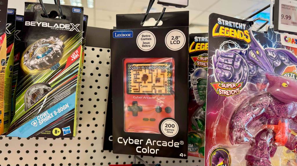 Eine rote getestete Retro-Spielekonsole hängt neben weiteren Spielzeugen an einem Verkaufsregal.