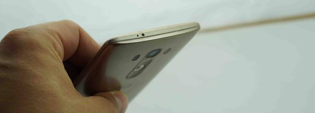 Android-Smartphone-Test: Hand hält das weiße Modell mit Fokus auf den oberen kurzen Rand und die rückseitige Hauptkamera vor weißem Hintergrund.