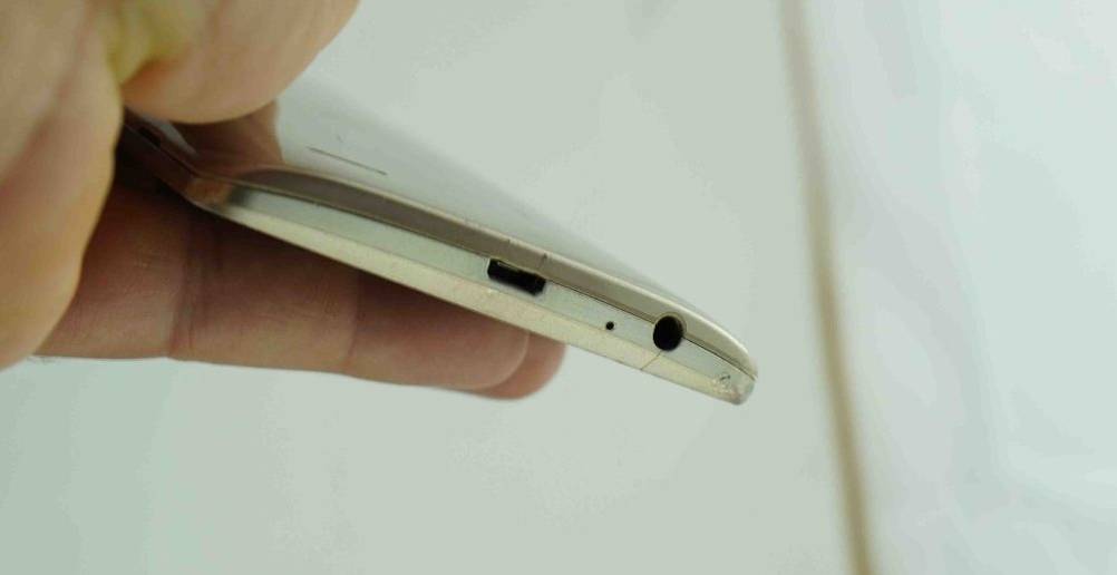 Android-Smartphone-Test: Hand hält das weiße Modell mit Fokus auf die Ladebuchse und den Kopfhöreranschluss vor weißer Fläche.