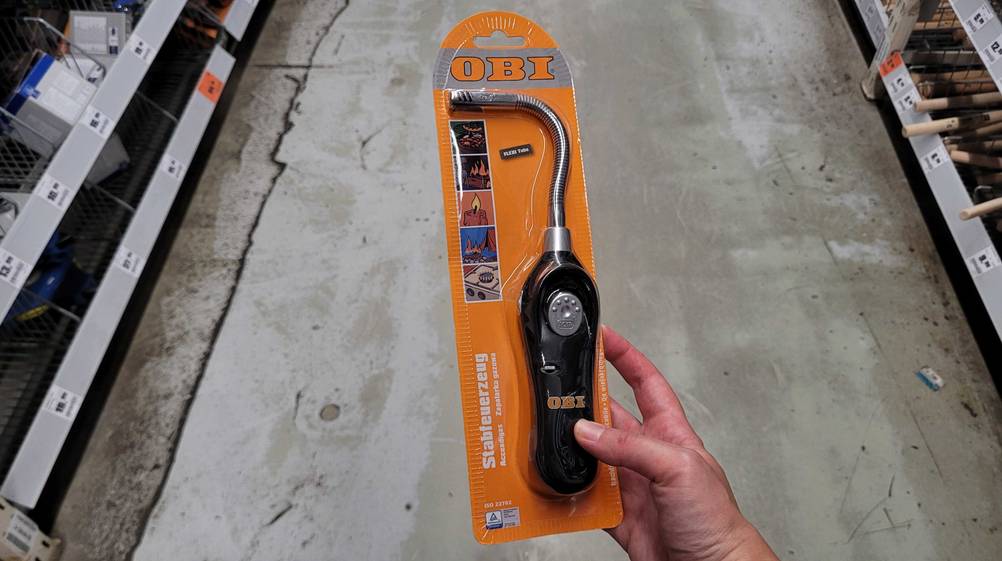 Lichtbogen-Feuerzeug getestet: Eine Hand hält ein originalverpacktes Lichtbogen-Feuerzeug über einen Betonboden.