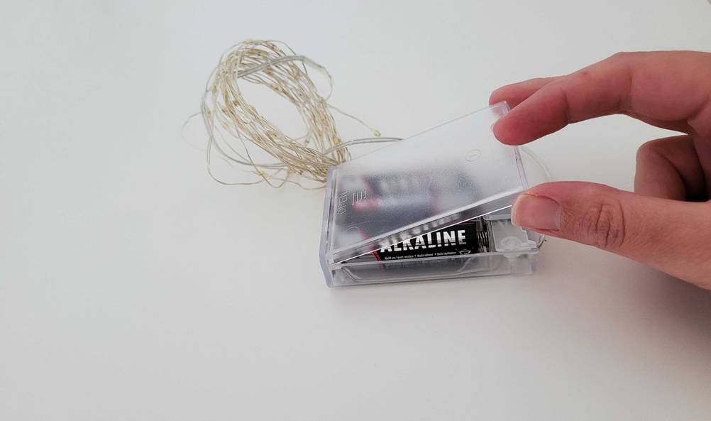 Lichterkette getestet: Eine Hand öffnet das Batteriefach einer Lichterkette.