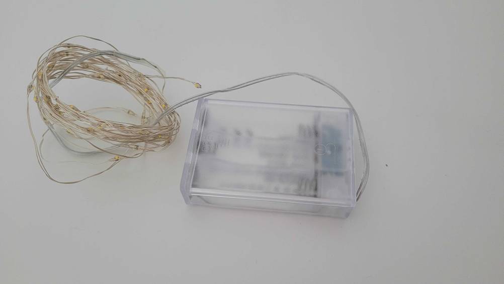 Eine getestete Lichterkette aus Draht mit leerem Batteriefach auf einer hellen Fläche.