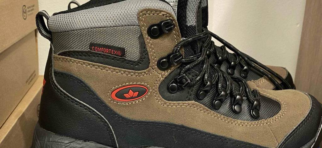 Seitenansicht, mit Fokus auf das verarbeitete Comfortex-Material, von beige-schwarzen Unisex-Bergschuhen im Test, die sich auf einem Verpackungskarton befinden.