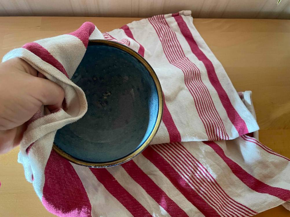 Eine Hand hält mit einem rot weiß gestreiften Geschirrtuch eine blaue Schüssel.