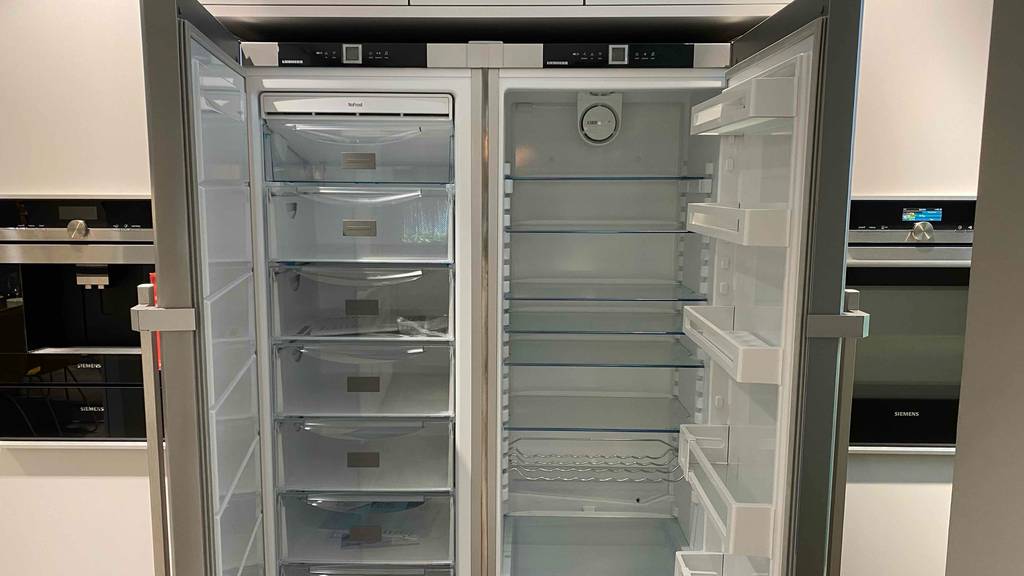Side-by-Side-Kühlschrank ohne Wasseranschluss im Test: Ansicht von vorn auf die Schubladen und Fächer eines geöffneten Modells in Anthrazit, das in einem Verkaufsbereich steht.